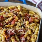 Cooked rotini pasta with tomatoes and prosciutto in a baking dish.