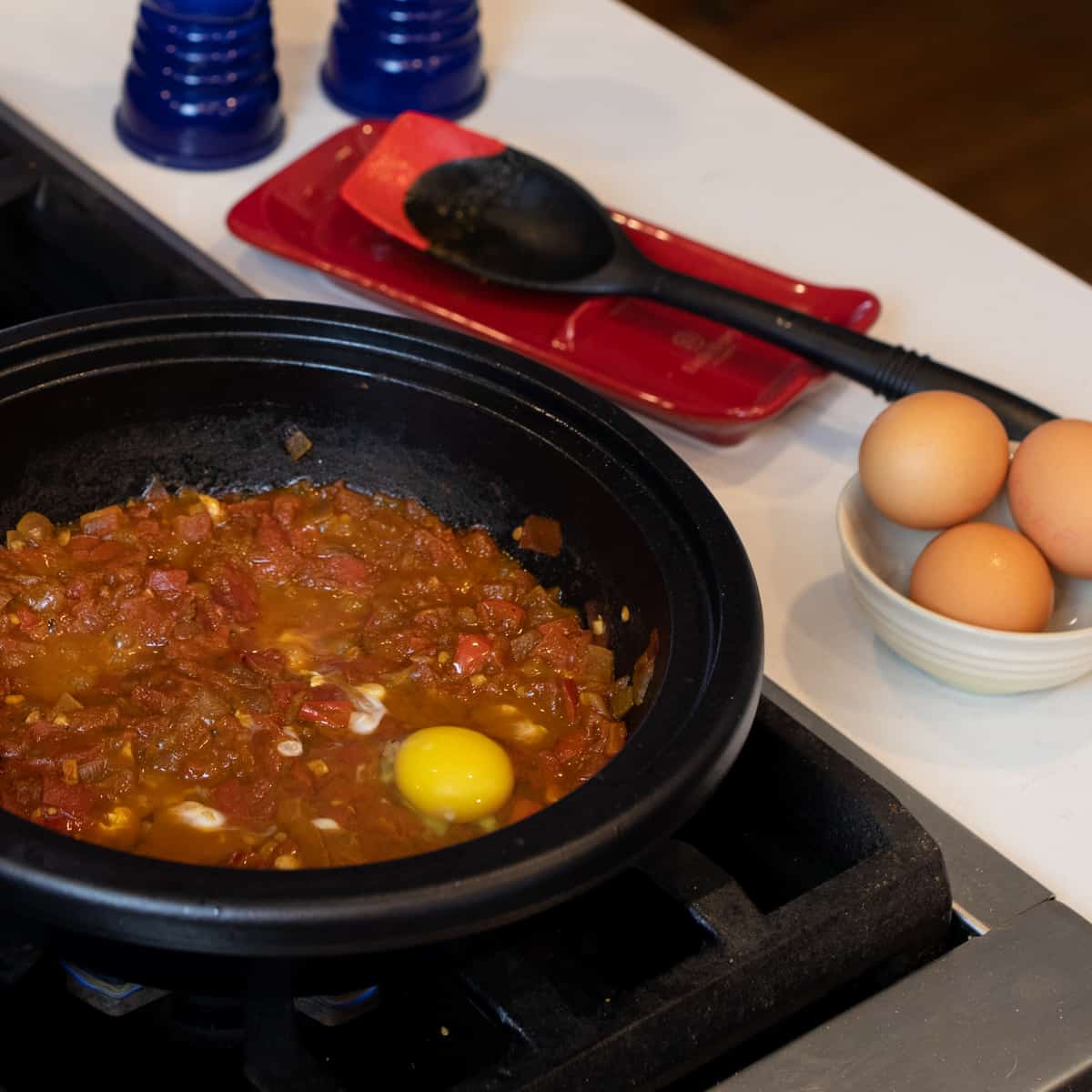 An egg freshly cracked on tomatoes simmering in a tagine base.
