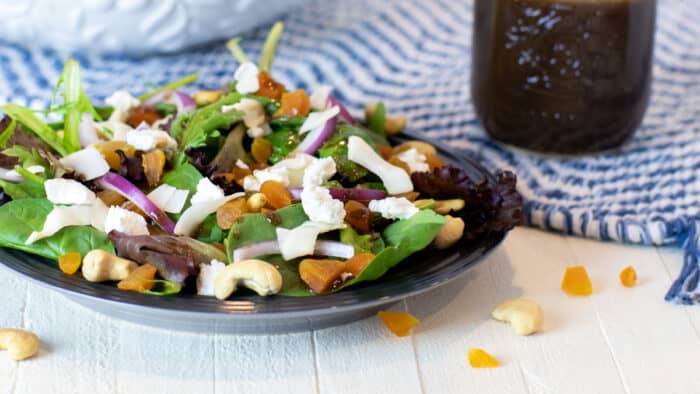 A plate of salad next to a jar of vinaigrette.