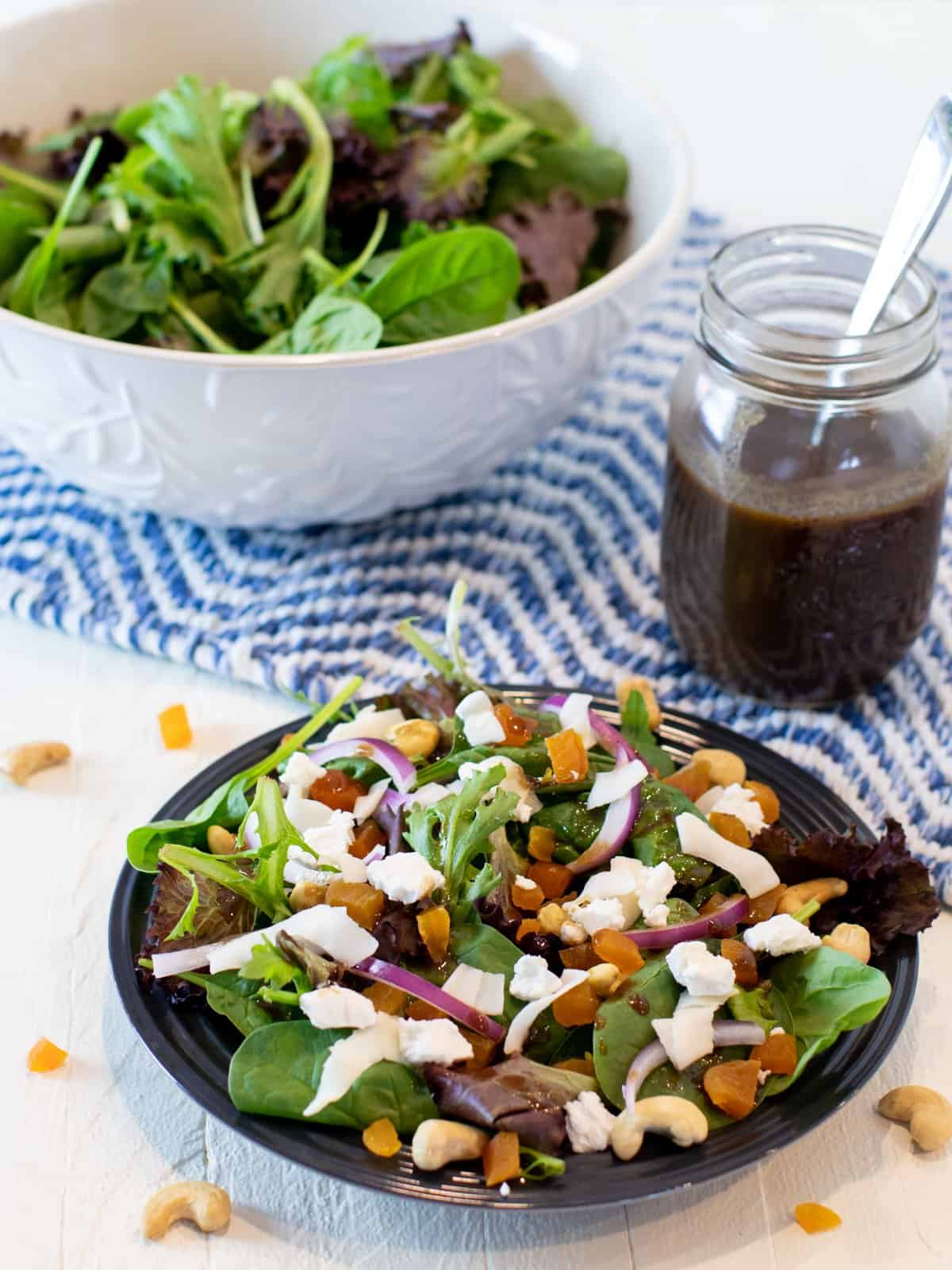 Overhead picture of a bowl and plate of salad with a jar of vinaigrette.