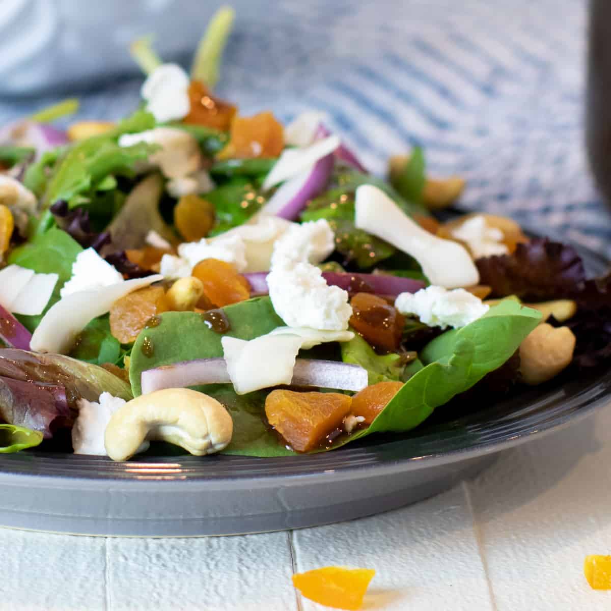 A close up of a plate of salad with spinach, apricot and cashews.