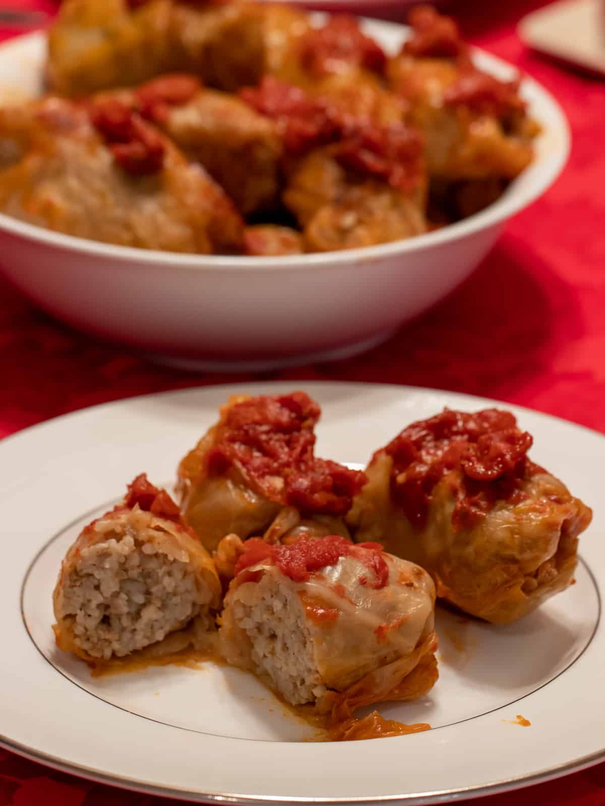 A plate of cabbage rolls with a serving bowl in the background holding more.