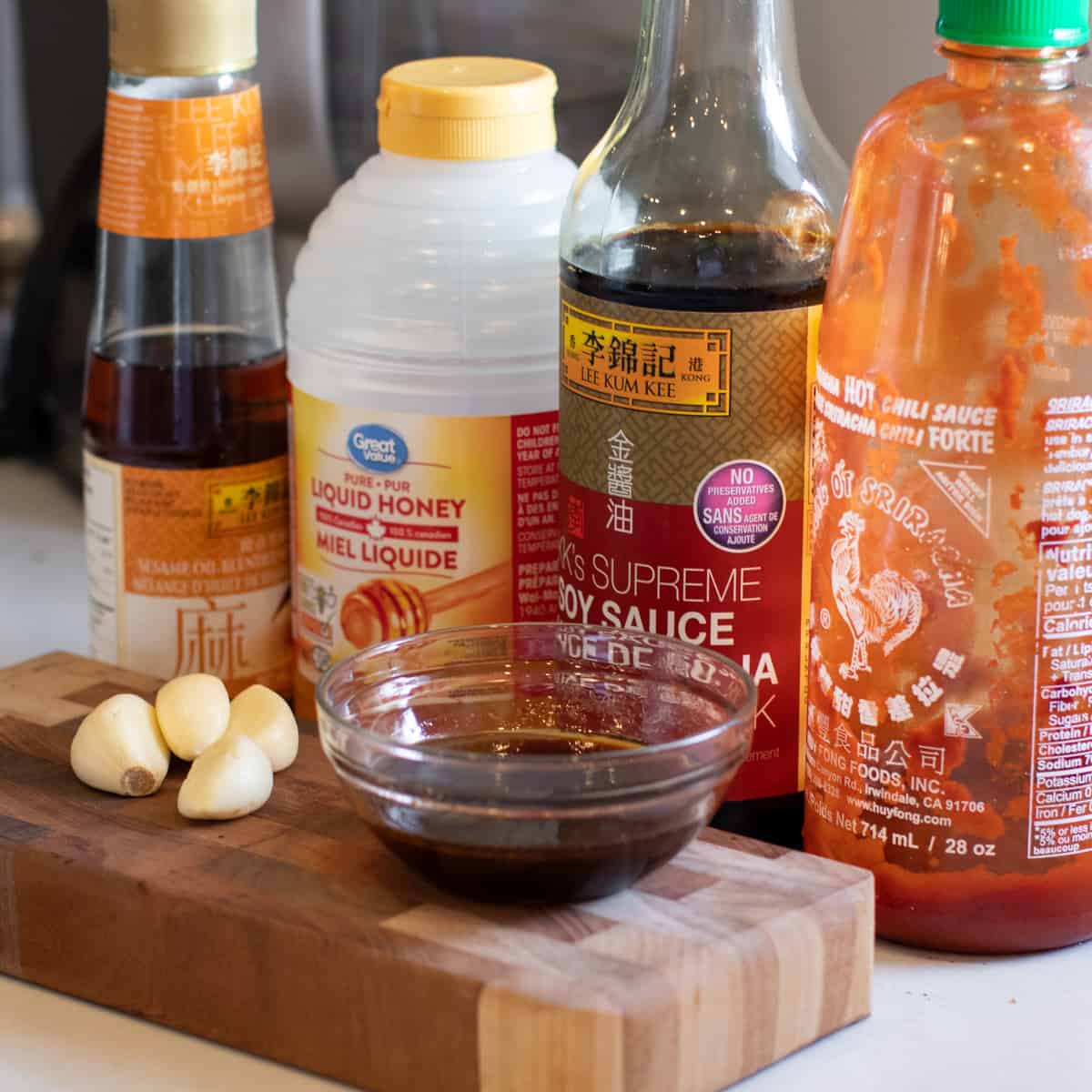 Ingredients for the sauce mixed in a small glass bowl next to a few cloves of garlic.