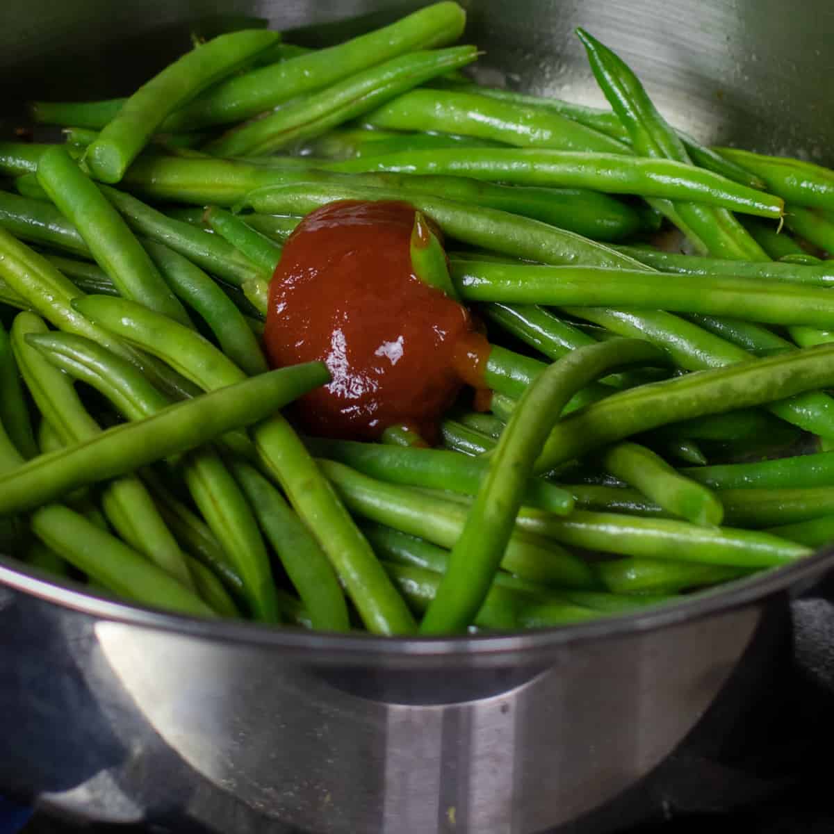 A spoonful of sriracha sauce on some raw green beans.