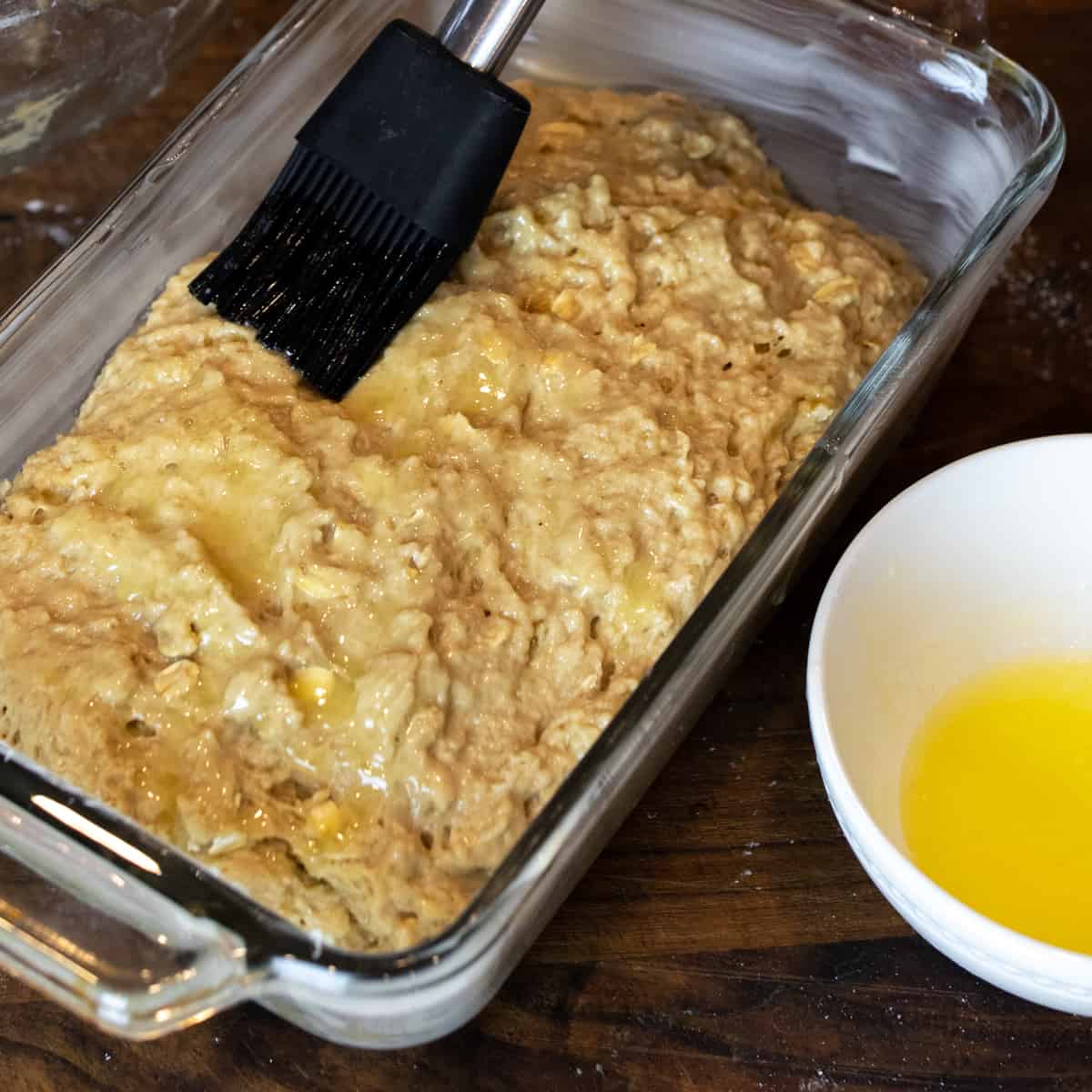 Melted butter being brushed onto batter in loaf pan.