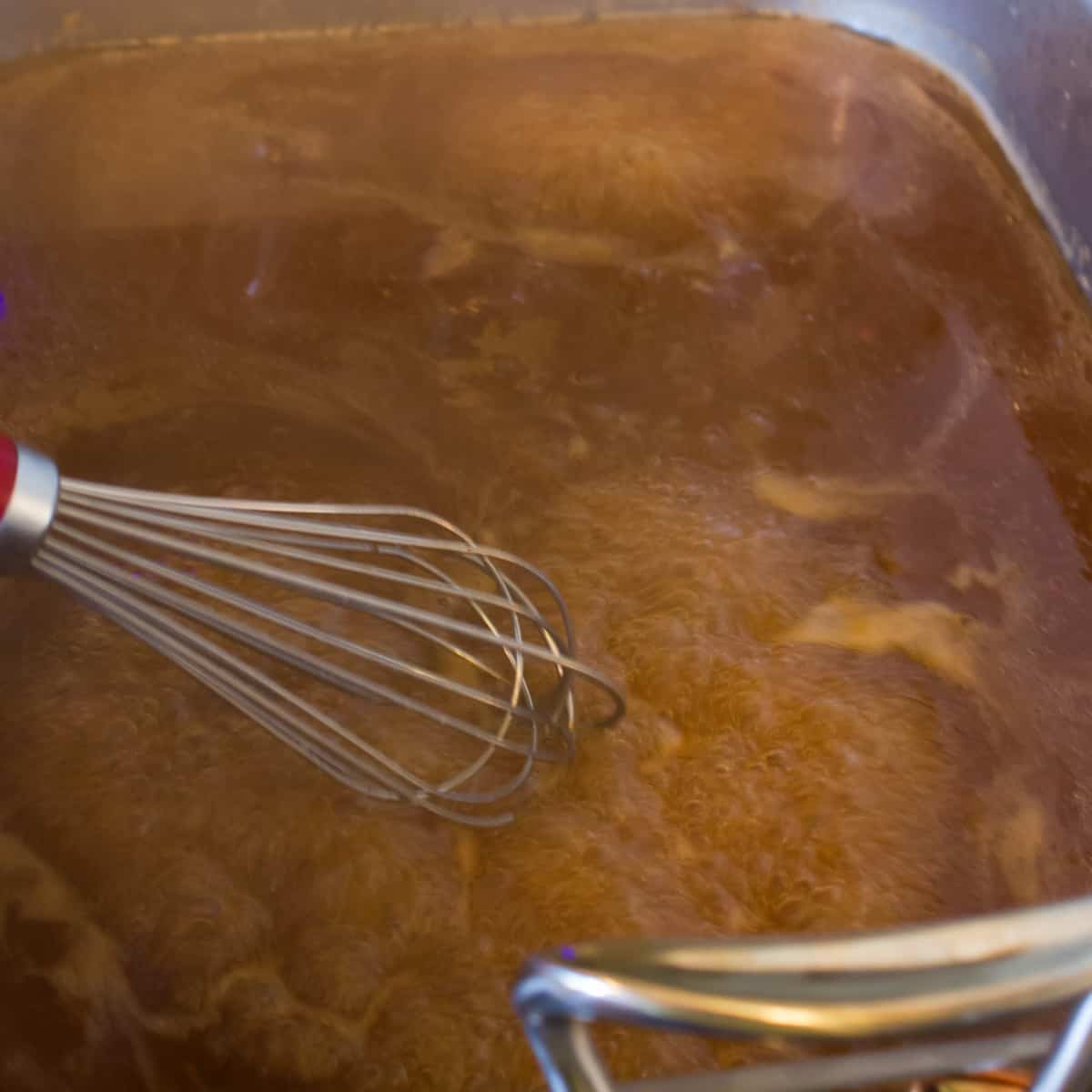 Gravy being stirred in a roaster rack.