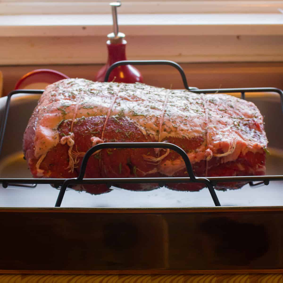 A raw beef roast on a roaster rack.