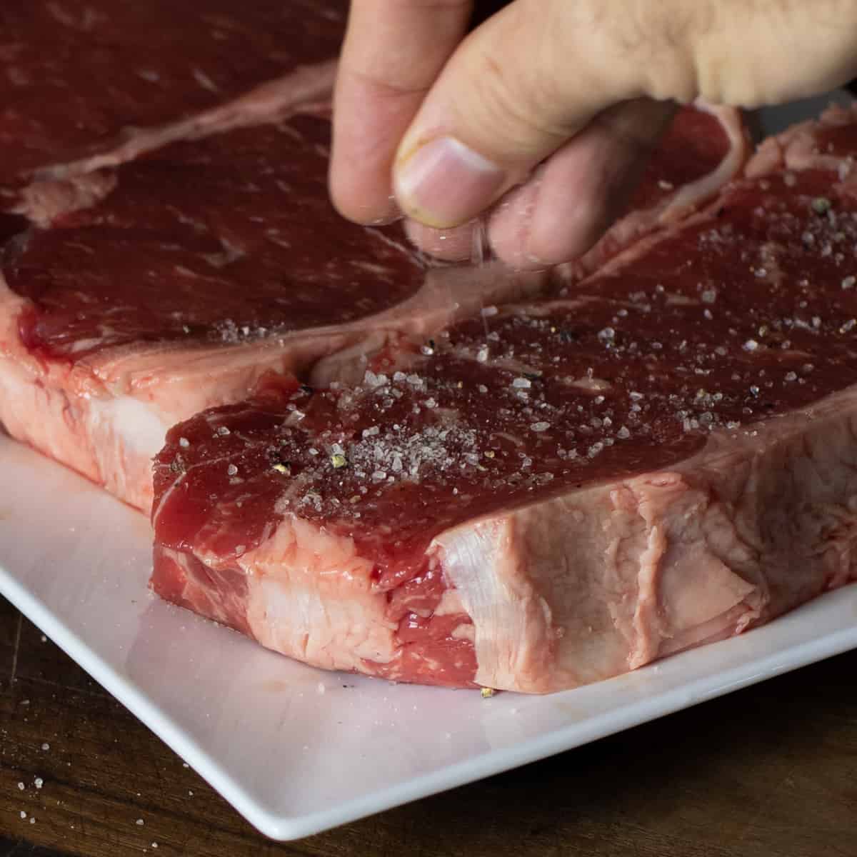Salt and pepper being sprinkled on a raw steak.
