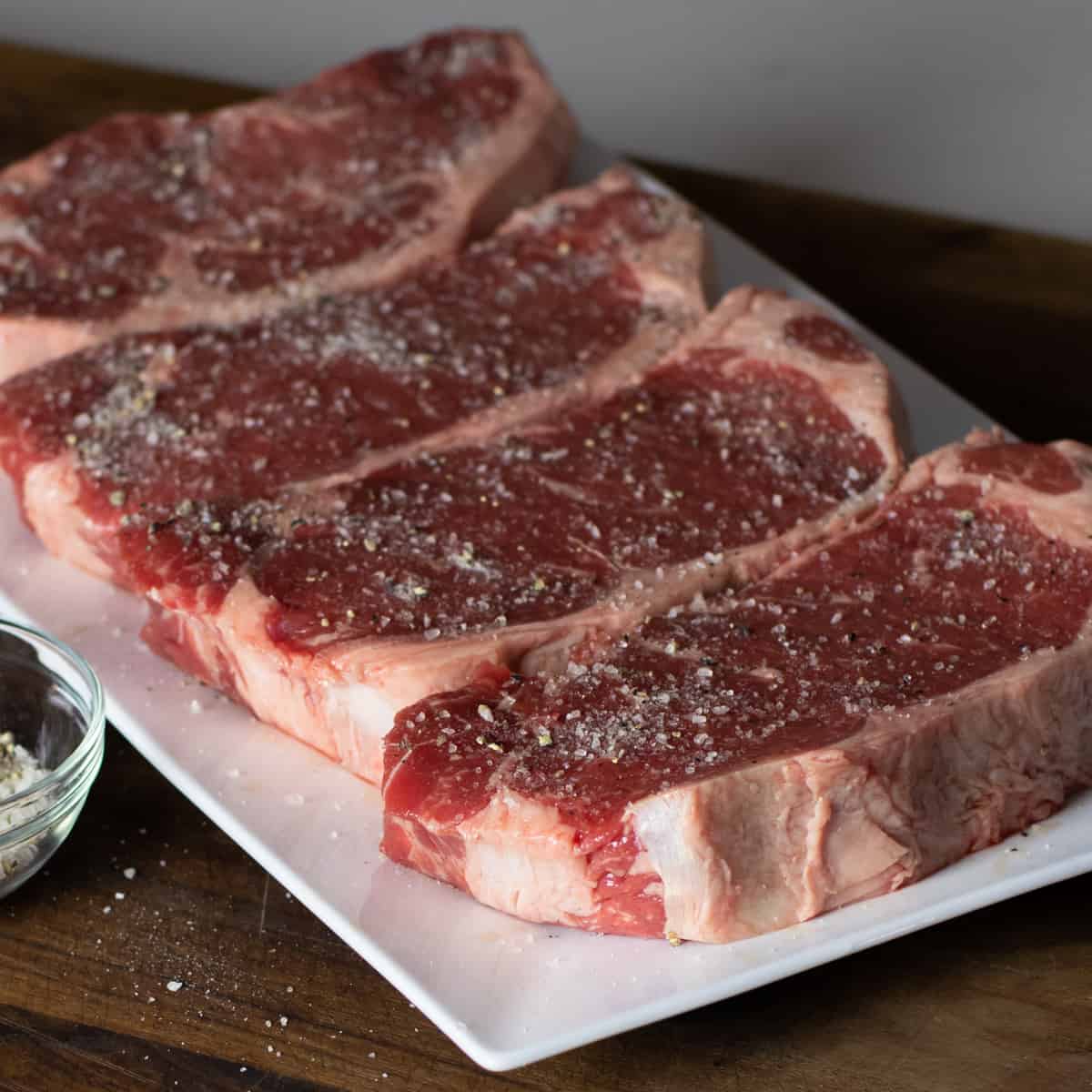 Seasoned steaks resting on a white platter.