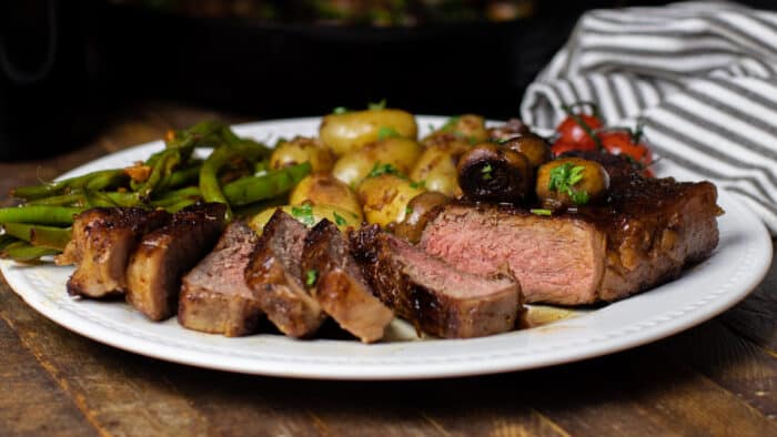 A sliced steak on a plate with potatoes and green beans.