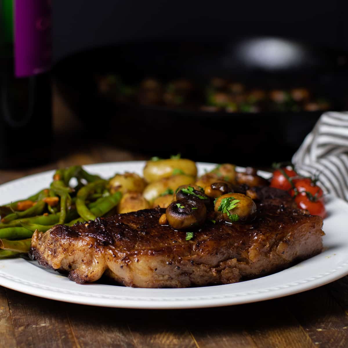 A whole pan seared steak on a plate with potatoes and green beans.