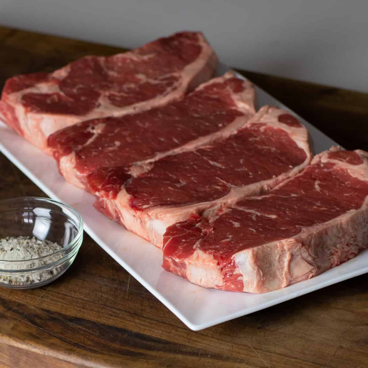 Four raw steaks on a white platter.