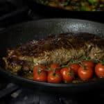 Cooked steak in a frying par with cherry tomatoes.