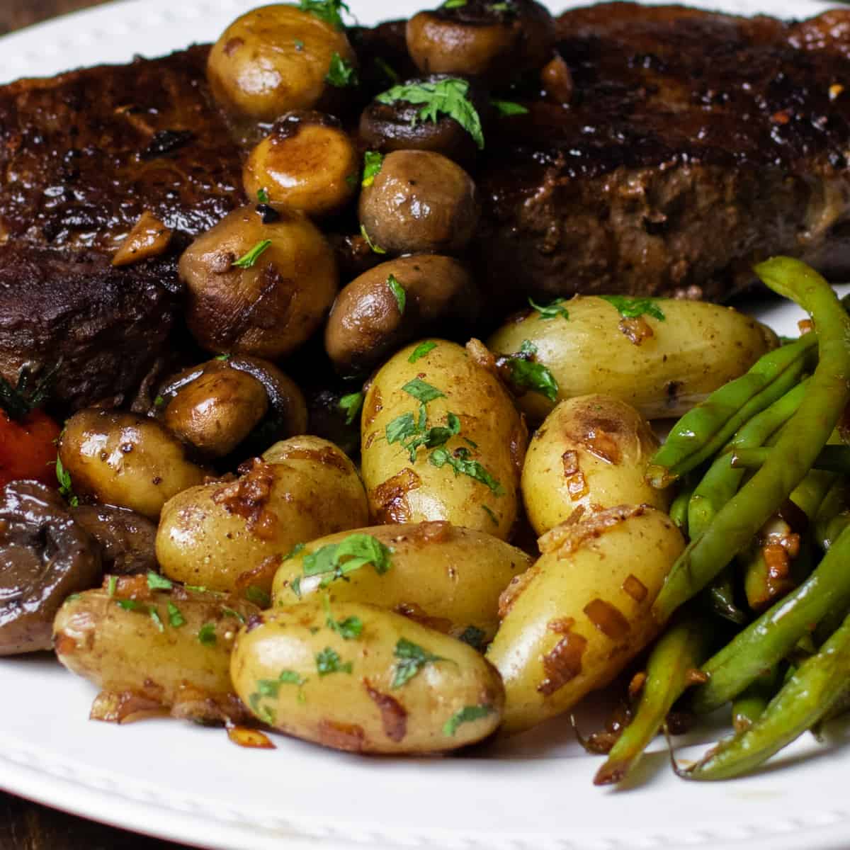 Fingerling potatoes on a plate with a steak, mushrooms and green beans.
