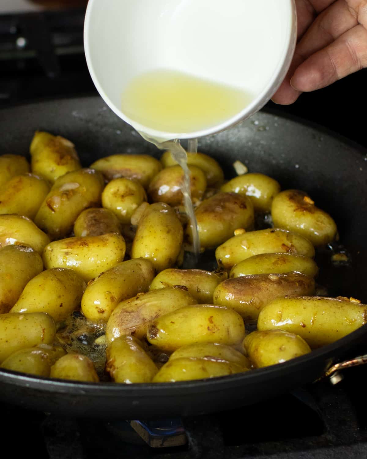 A white bowl of lemon juice being poured over potatoes.