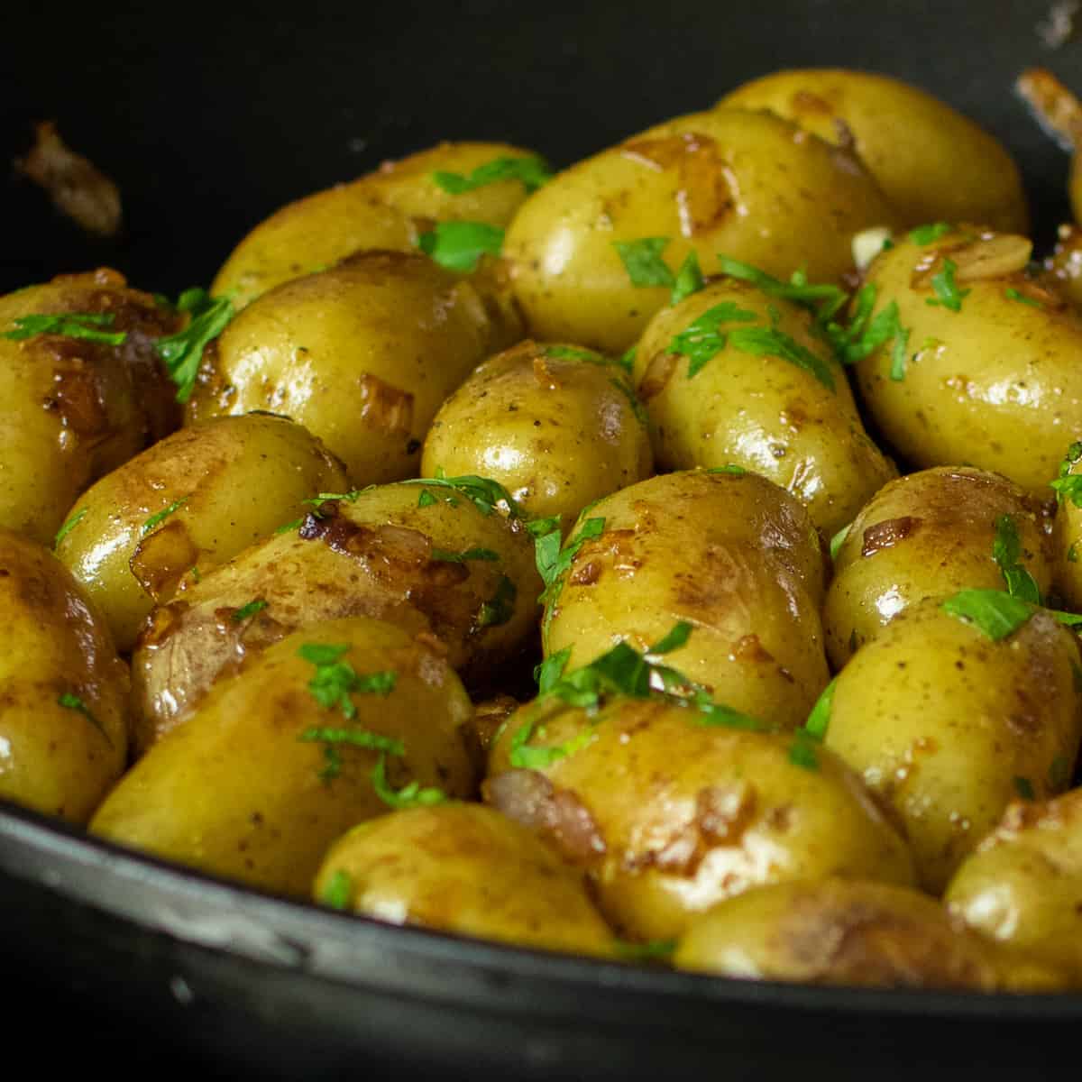 Cooked baby potatoes in a frying pan with fresh parsley sprinkled on top.