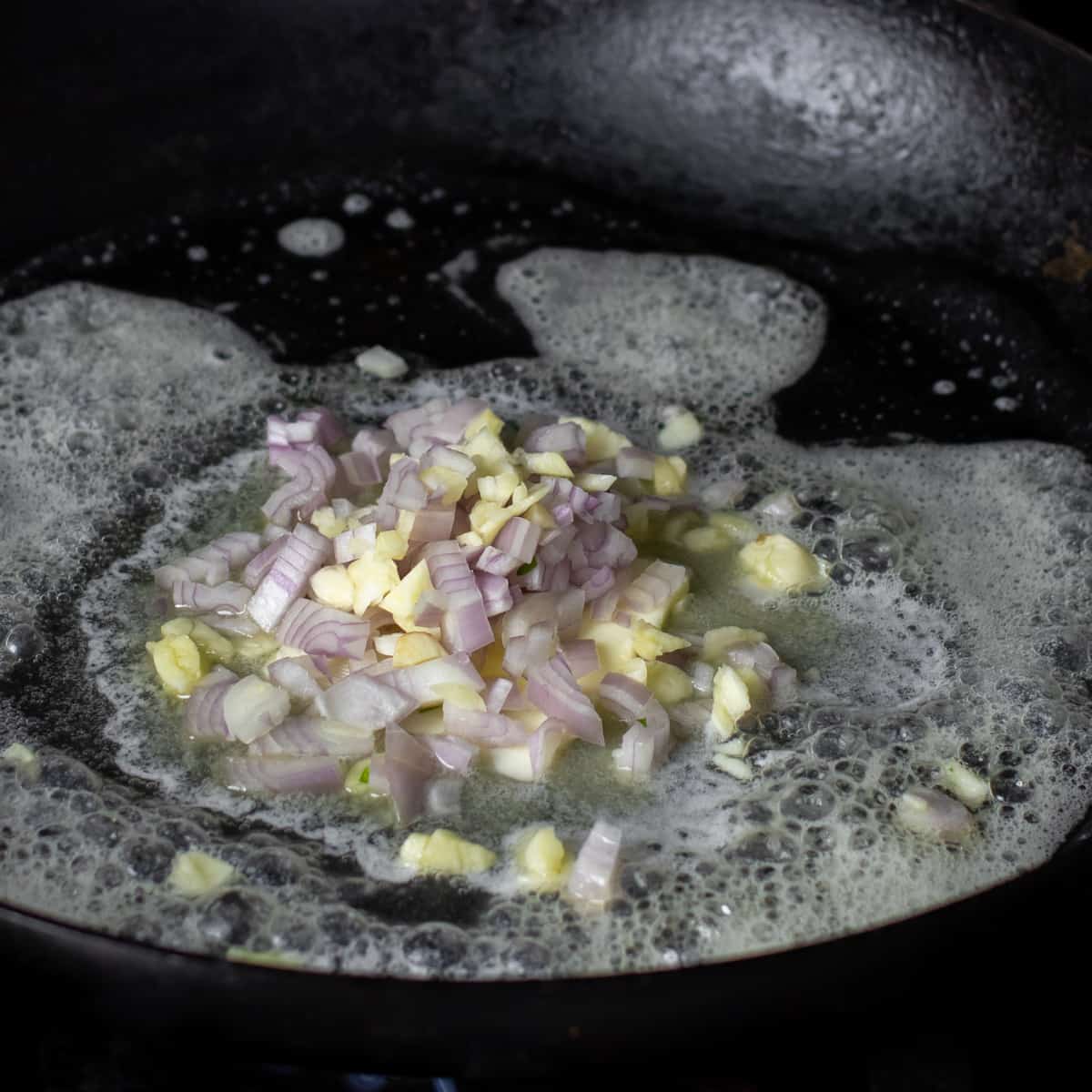 A minced shallot and garlic in a frying pan with melted butter.