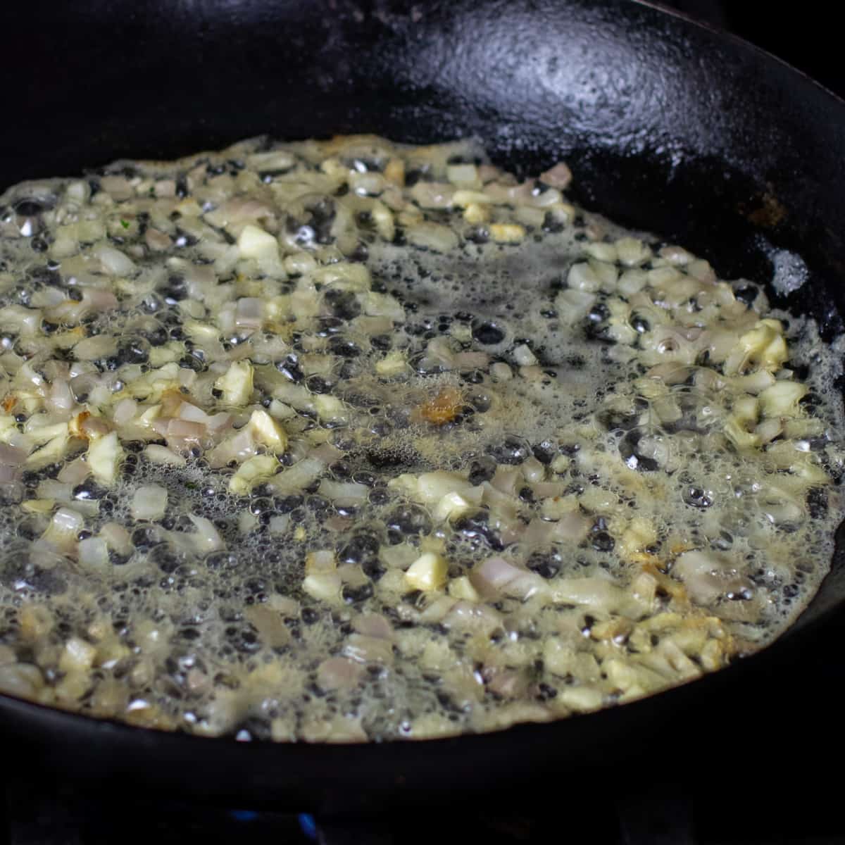 A minced shallot and garlic sautéing in a frying pan.