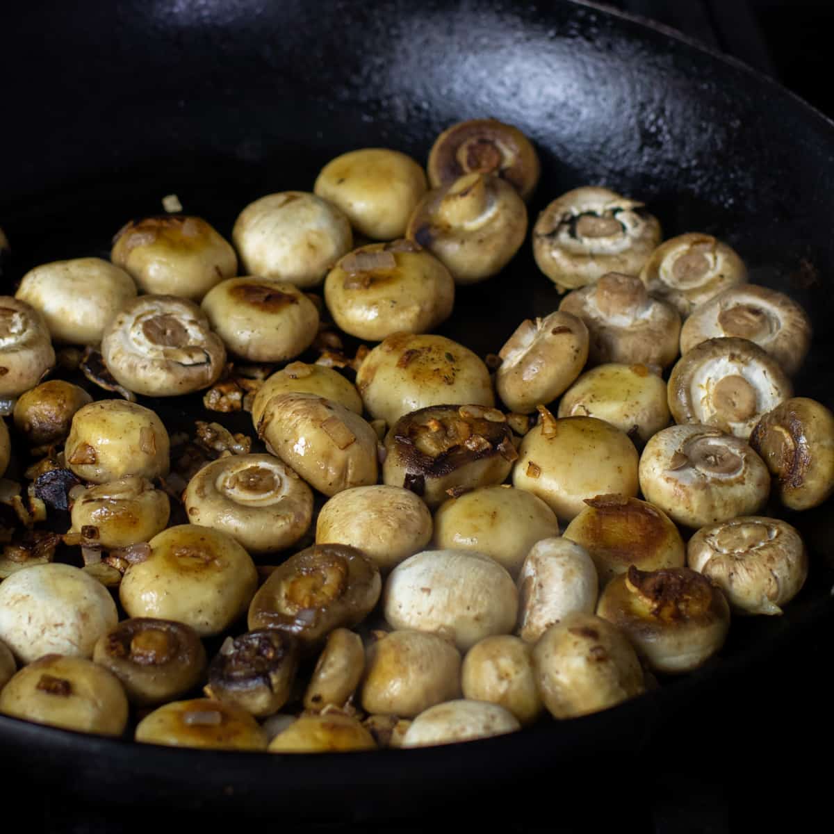 Button mushrooms cooking in a frying pan.