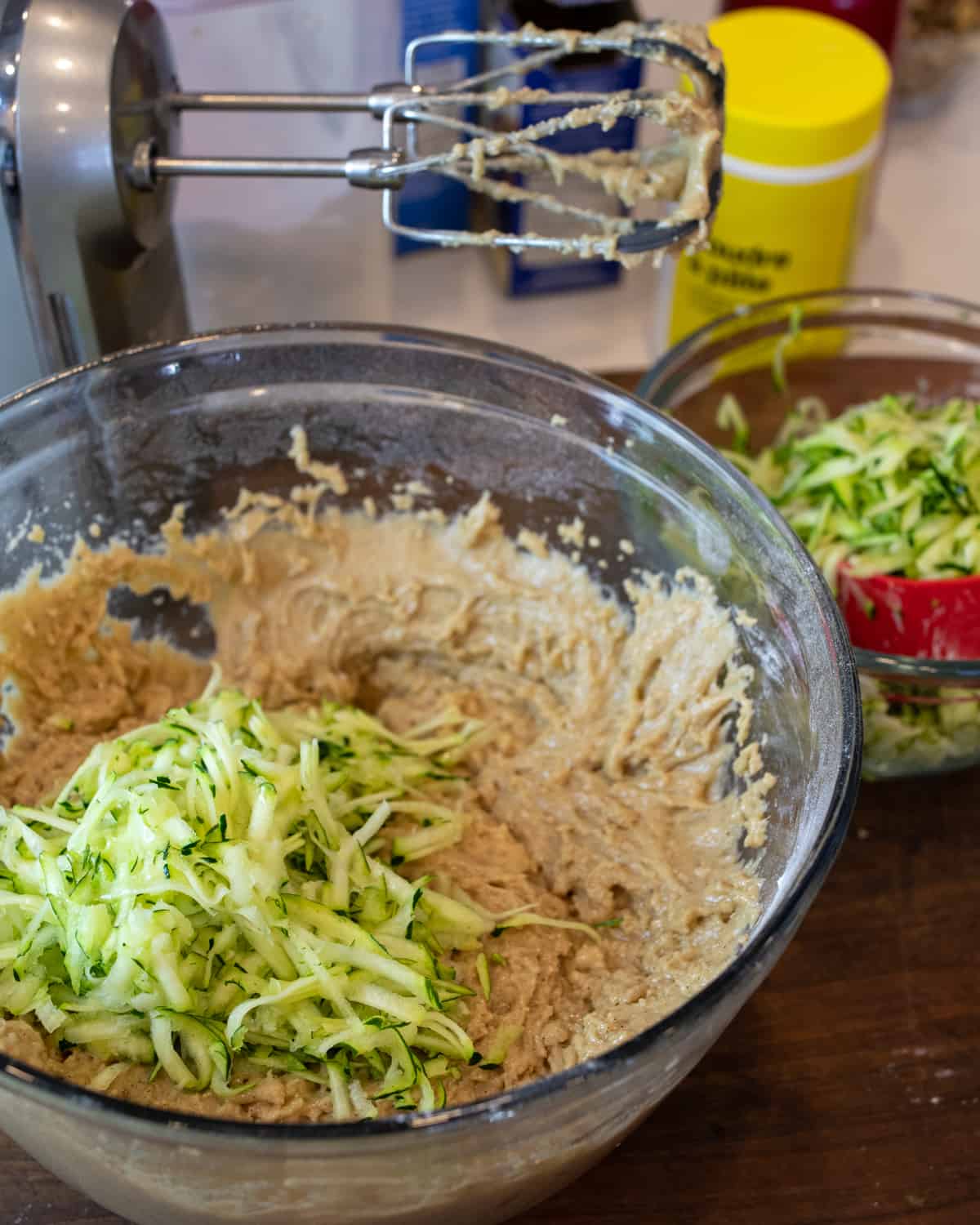 Batter in a glass bowl with a pile of grated zucchini on top.