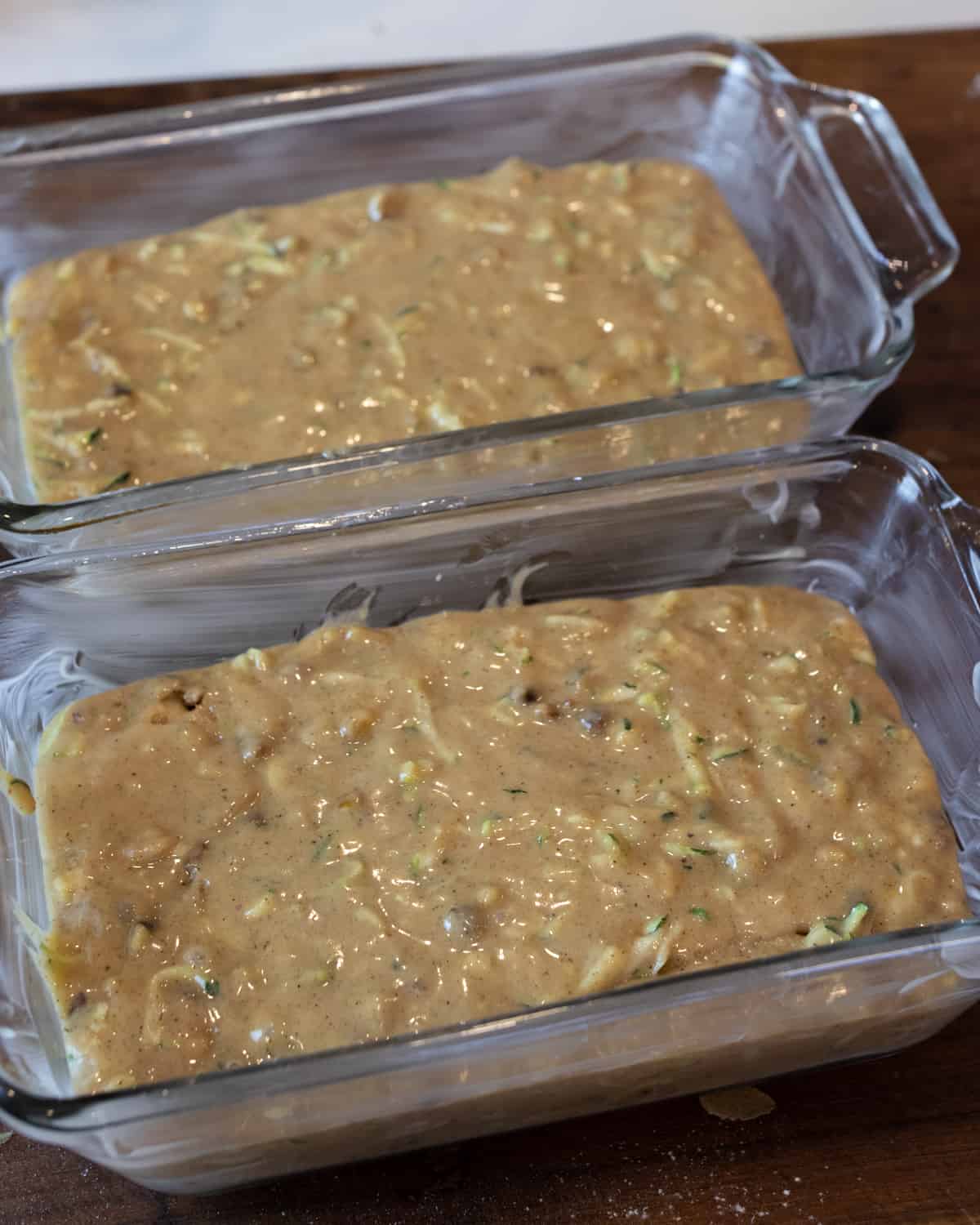 Two glass loaf pans that have raw batter poured into them.