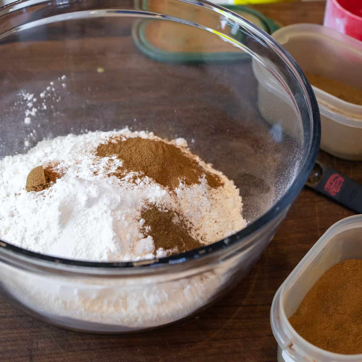 Flour, cinnamon and other dry ingredients dumped into a glass mixing bowl.
