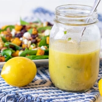A jar of homemade lemon salad dressing in front of a plate of fresh salad.