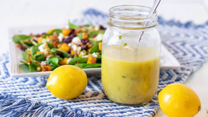 A jar of homemade lemon salad dressing in front of a plate of fresh salad.