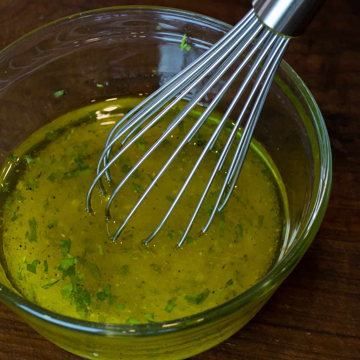 A whisk with dressing ingredients in a glass bowl.