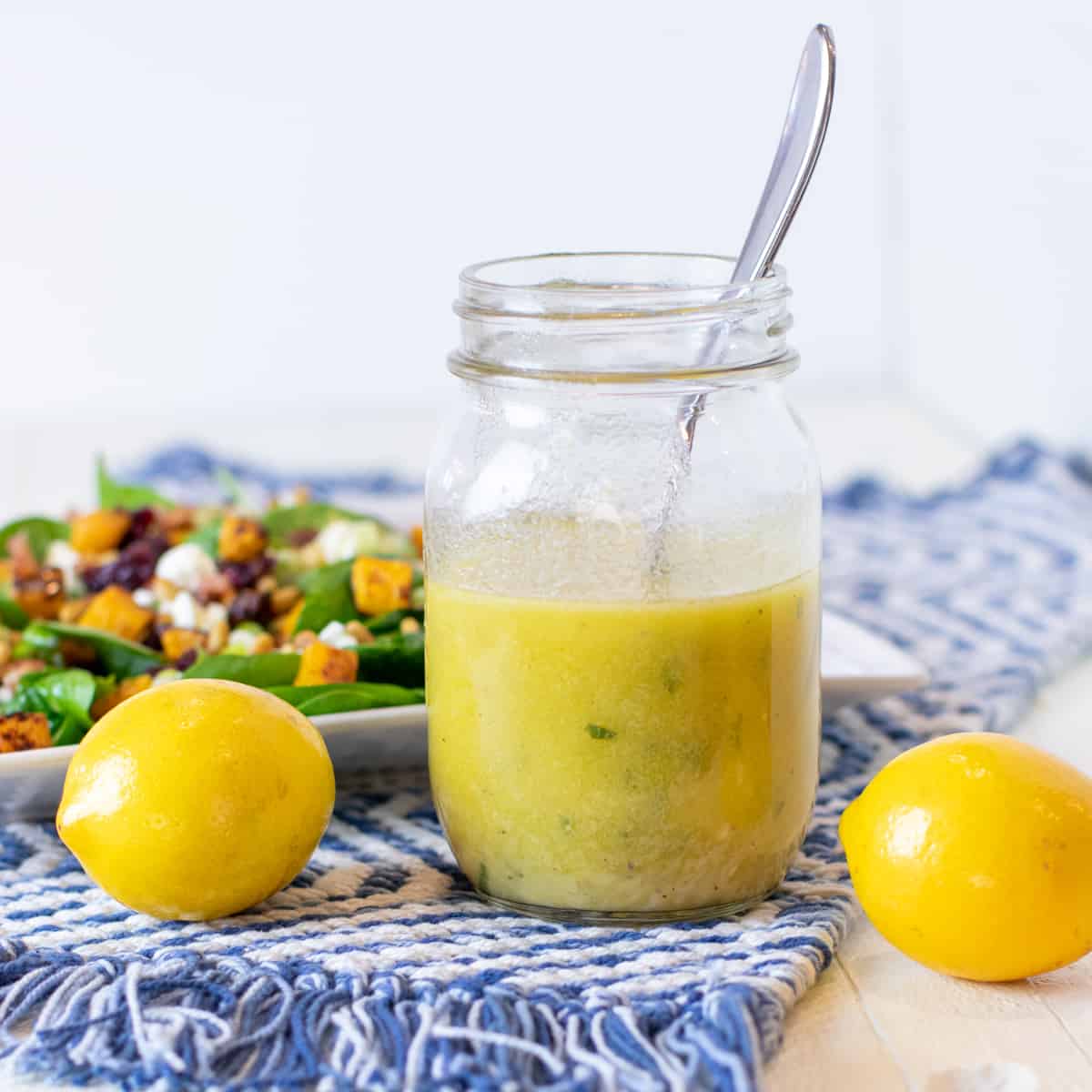 Lemon vinaigrette in a jar next to two whole lemons.