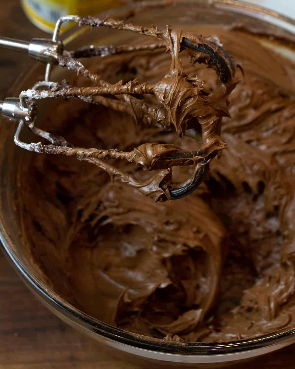 Chocolate icing just mixed in a glass bowl with icing on the beaters.