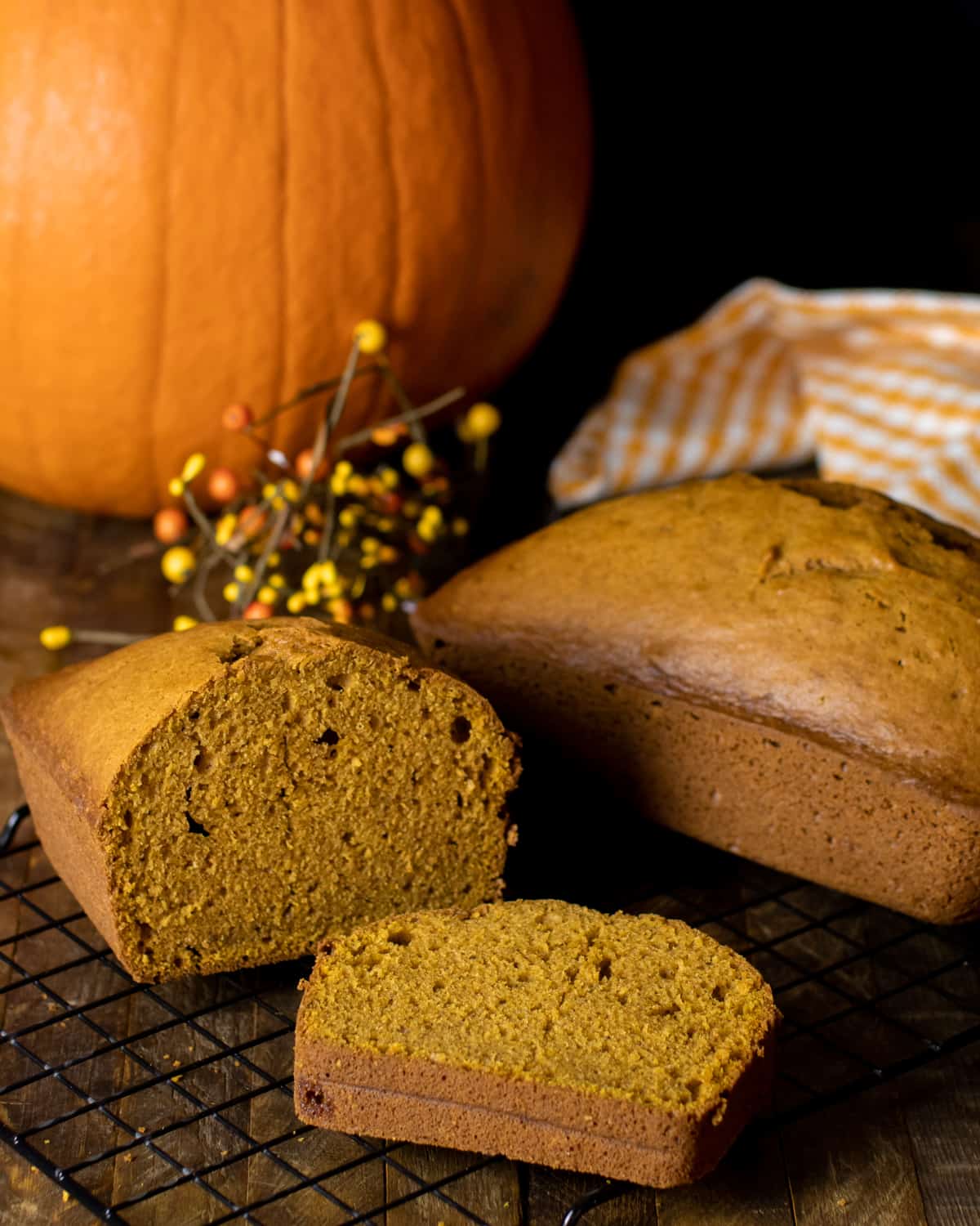 Two pumpkin loaves in front of a fresh whole pumpkin.