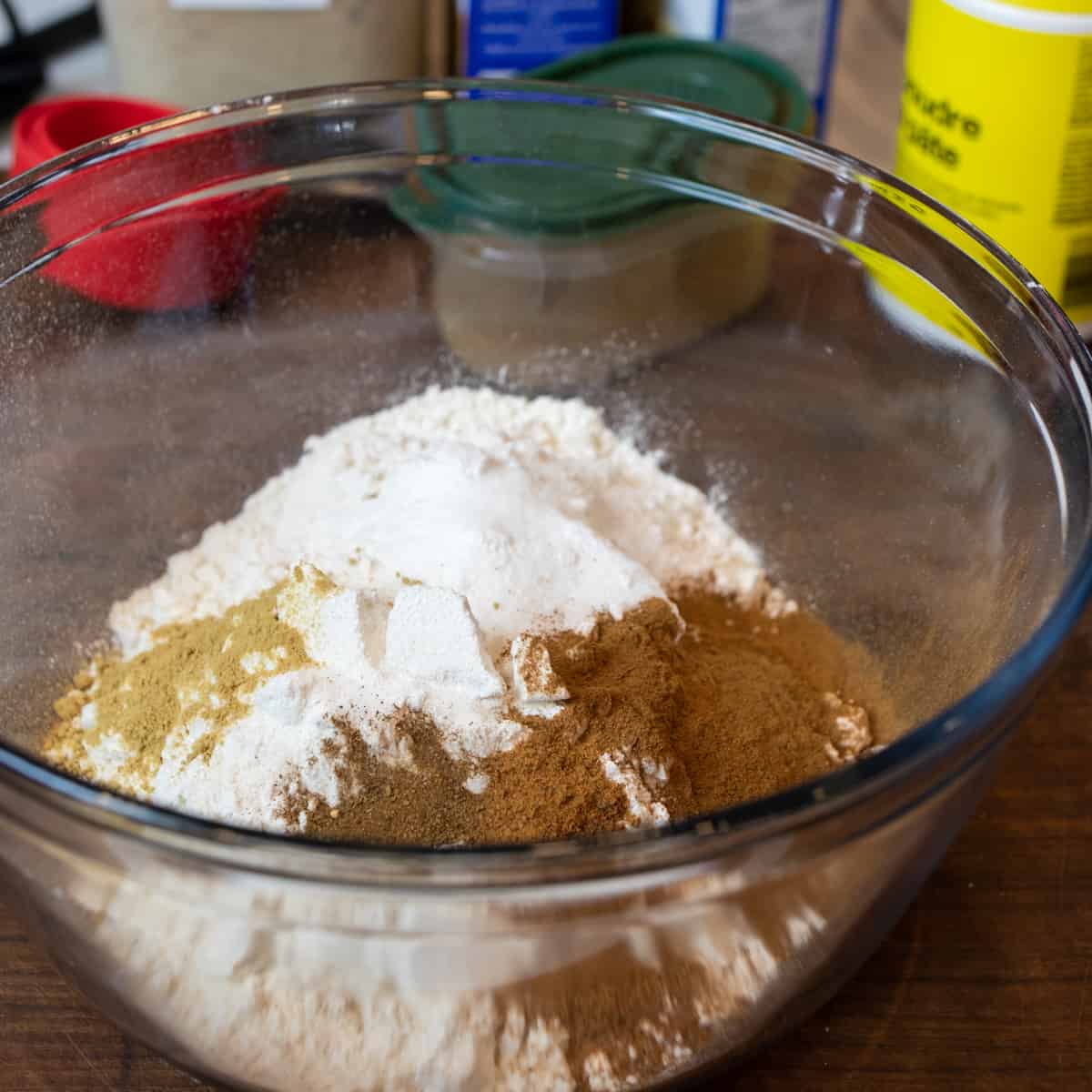 A glass bowl filled with flour, baking powder, baking soda and spices.