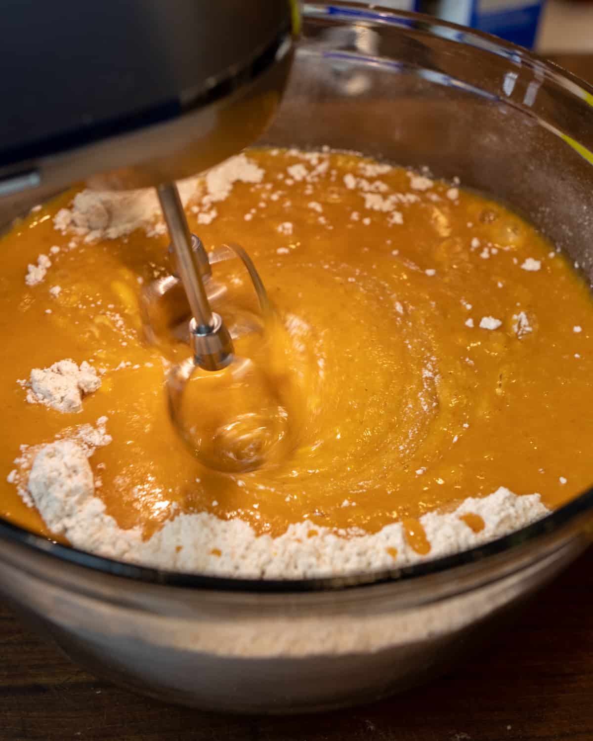 Electric mixer beating the wet and dry ingredients together in a mixing bowl.