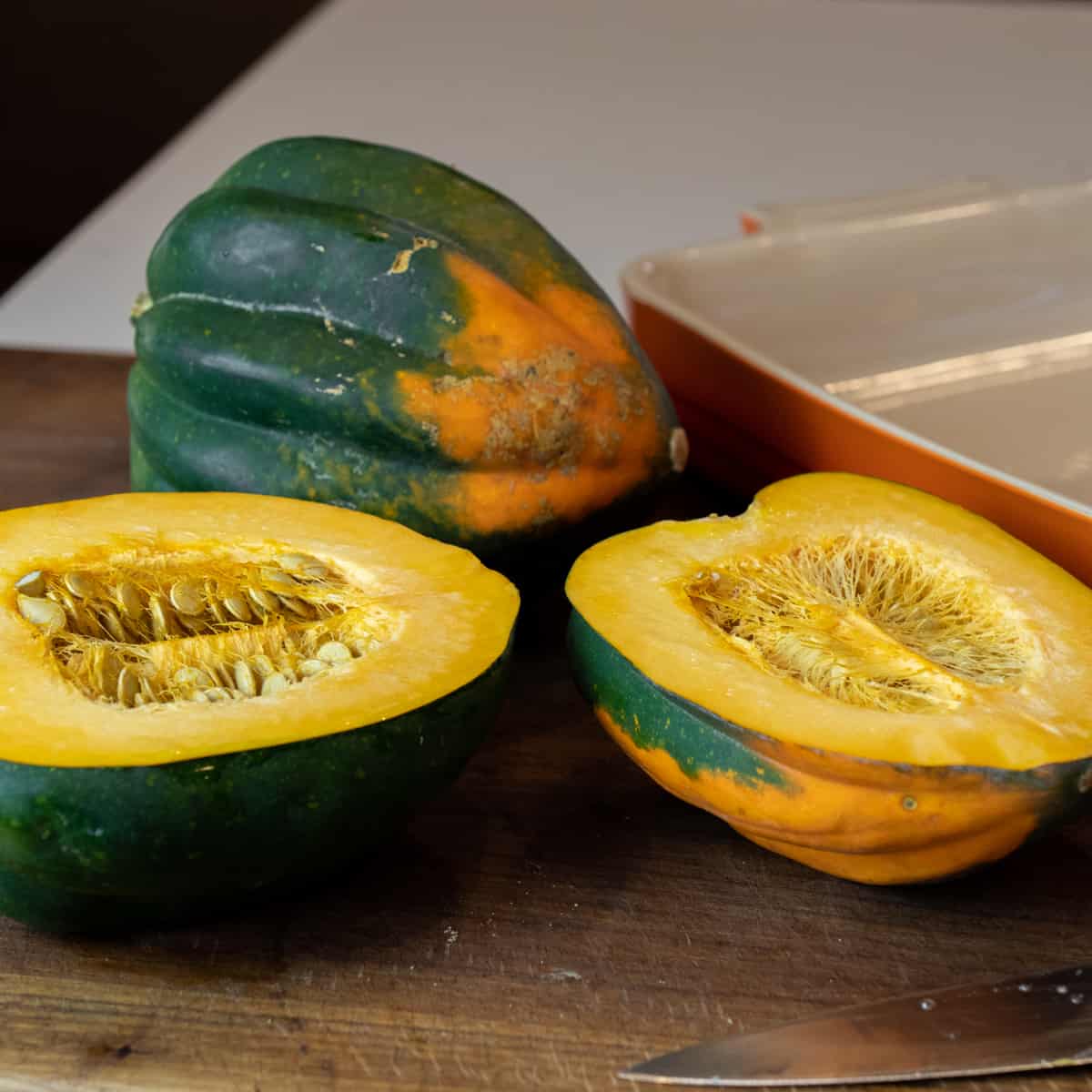 Acorn squash cut in half next to a whole one.