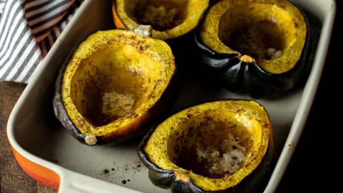 Cooked acorn squash halves in a baking dish.