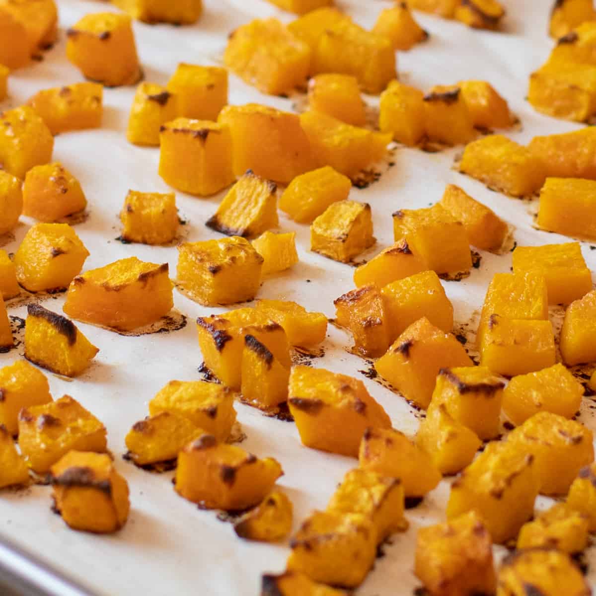 Cooked pieces of squash on a baking sheet lined with parchment paper.