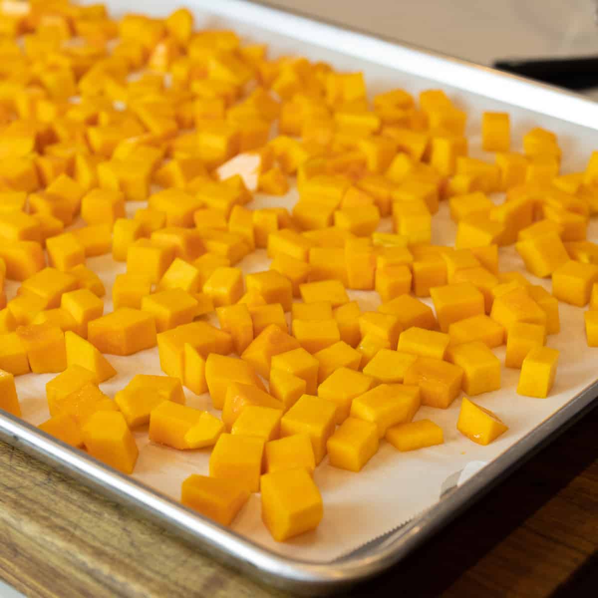 Cubes of butternut squash spread out evenly on a baking sheet.