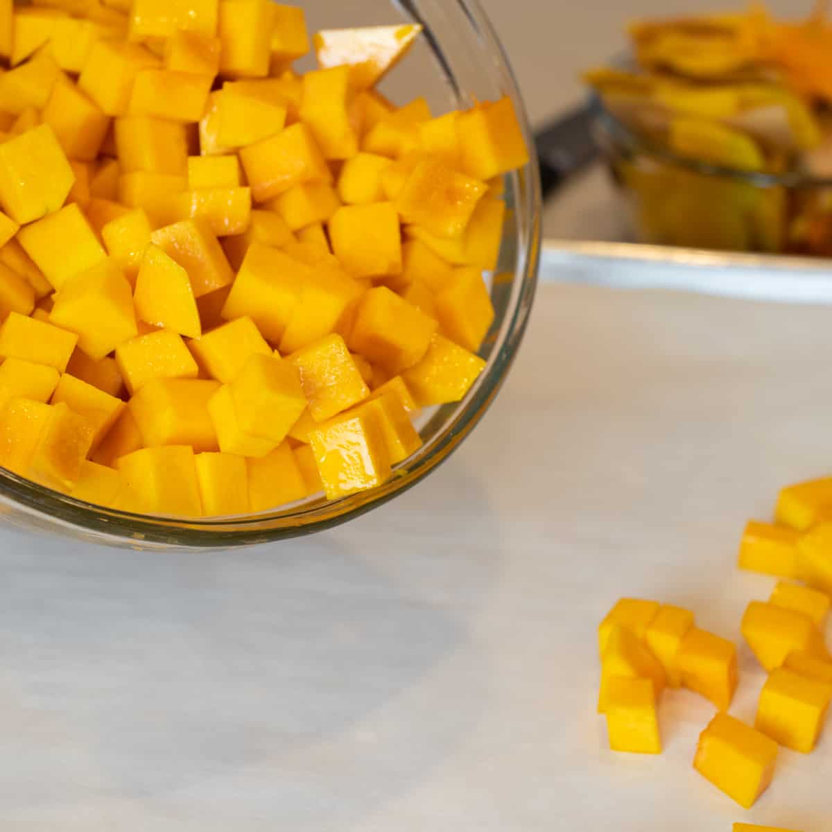 Squash chunks being spread onto a baking beet lined with parchment paper.