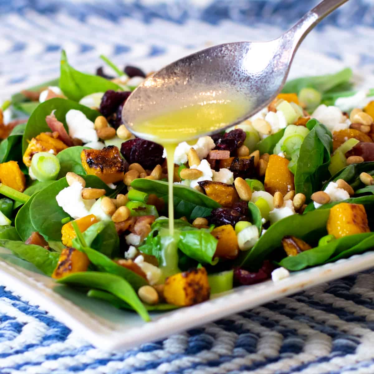 A spoonful of lemon vinaigrette being drizzled onto a salad.