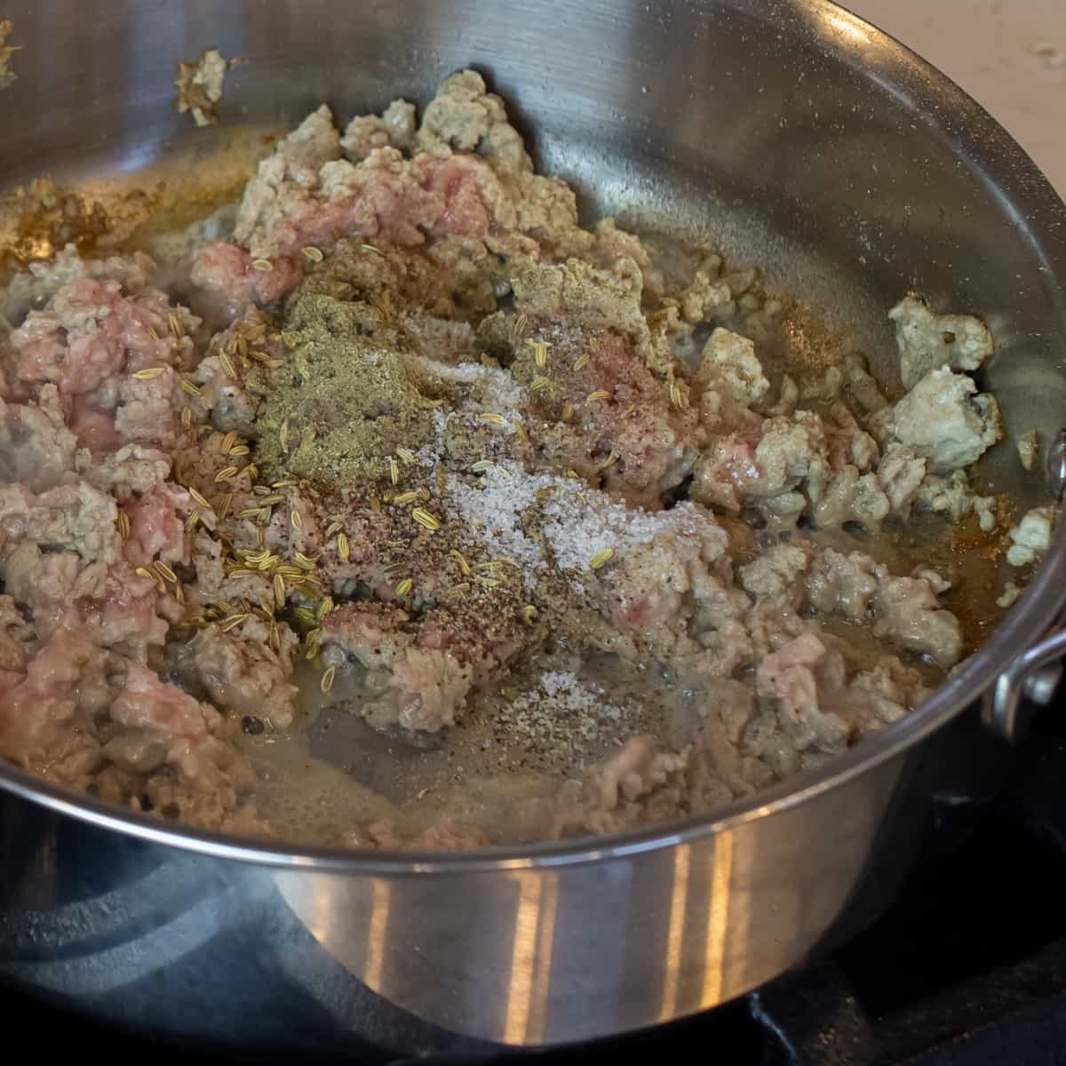 Spices on cooked ground chicken in a skillet.