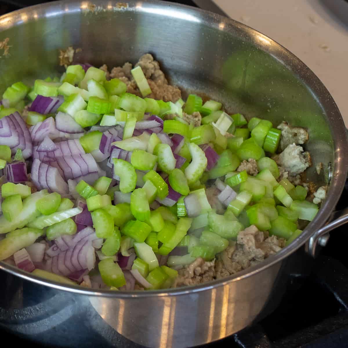 A skillet with chopped raw celery and onion on cooked turkey.