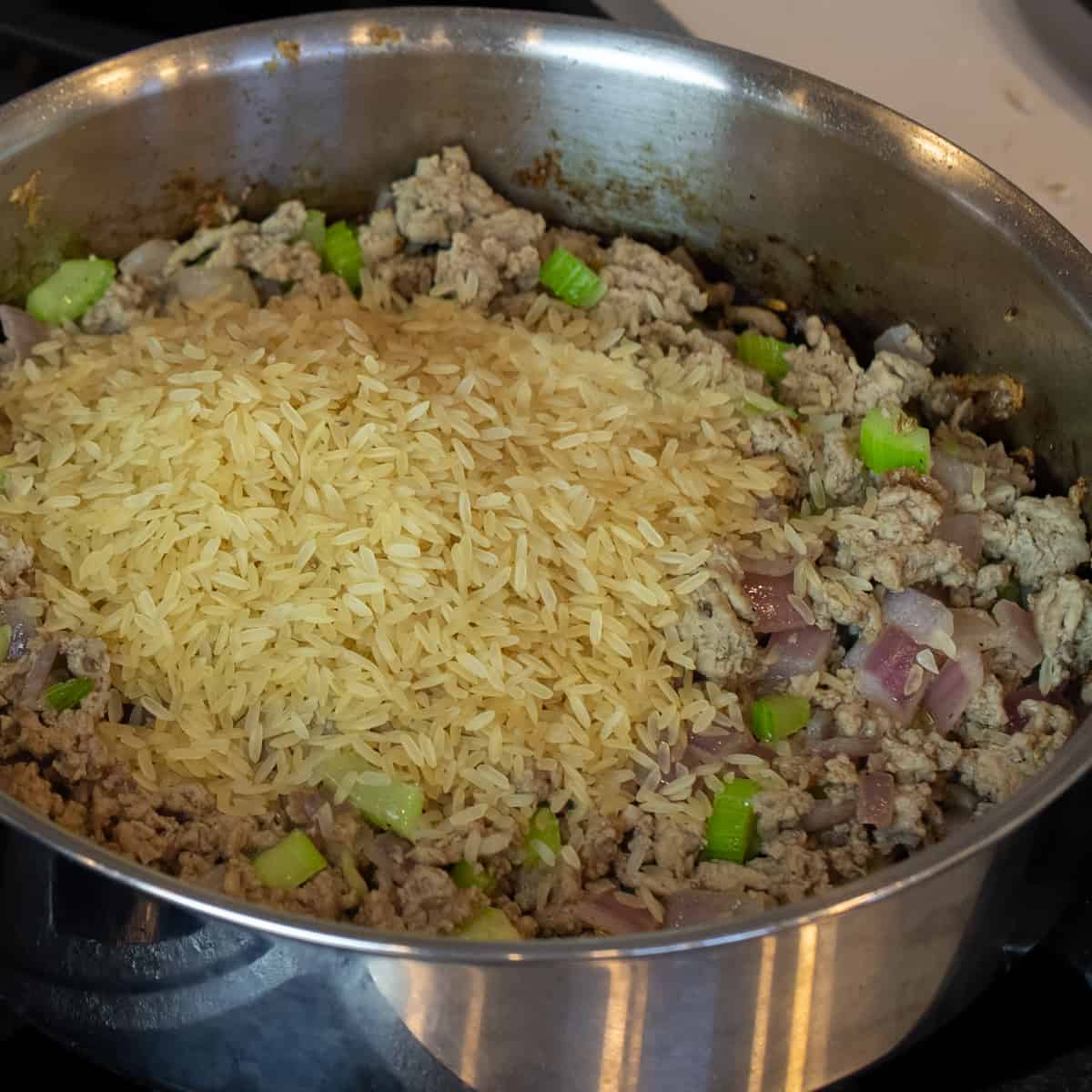 Raw rice added to a skillet with cooked turkey.