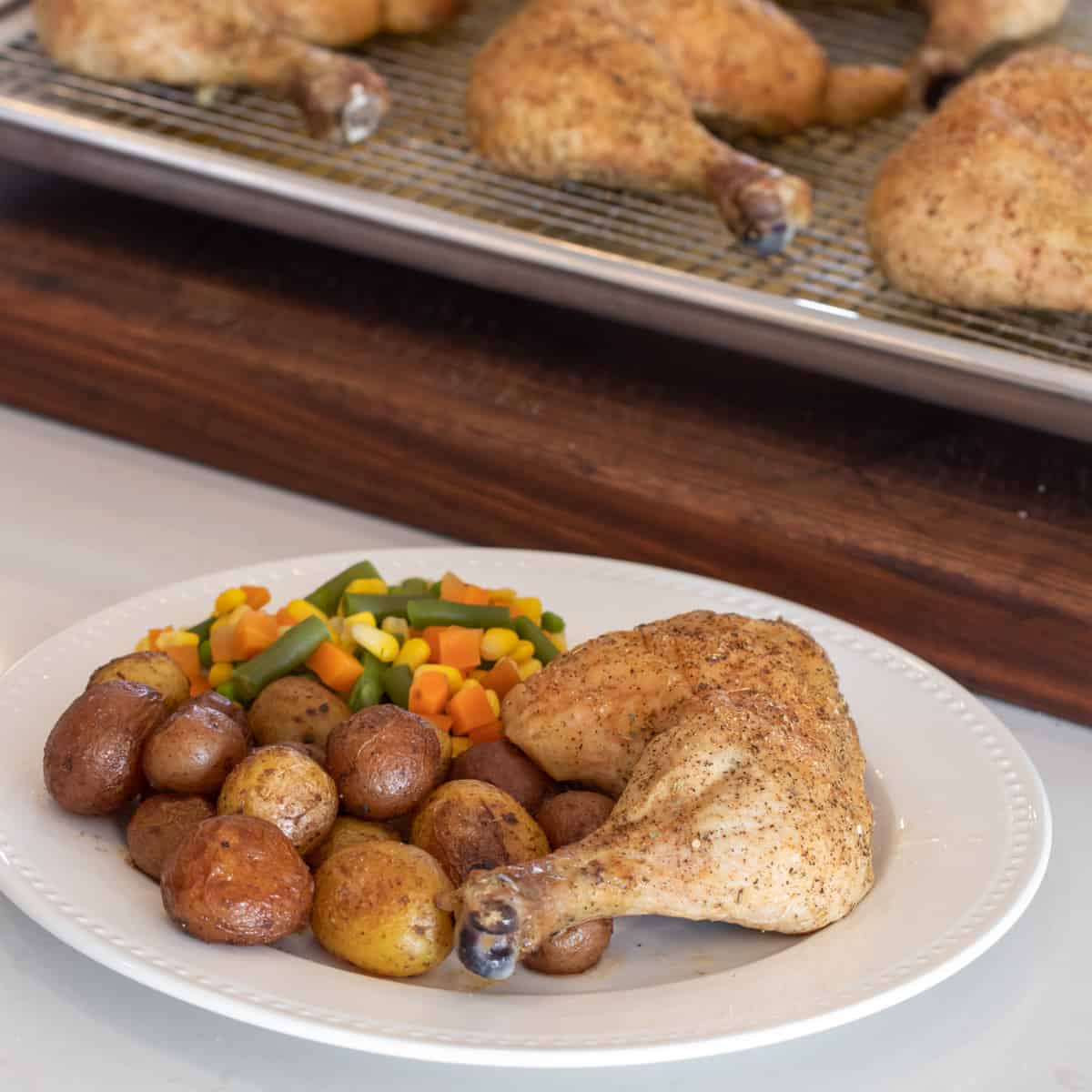 A round white plate with cooked chicken, potatoes and vegetables.