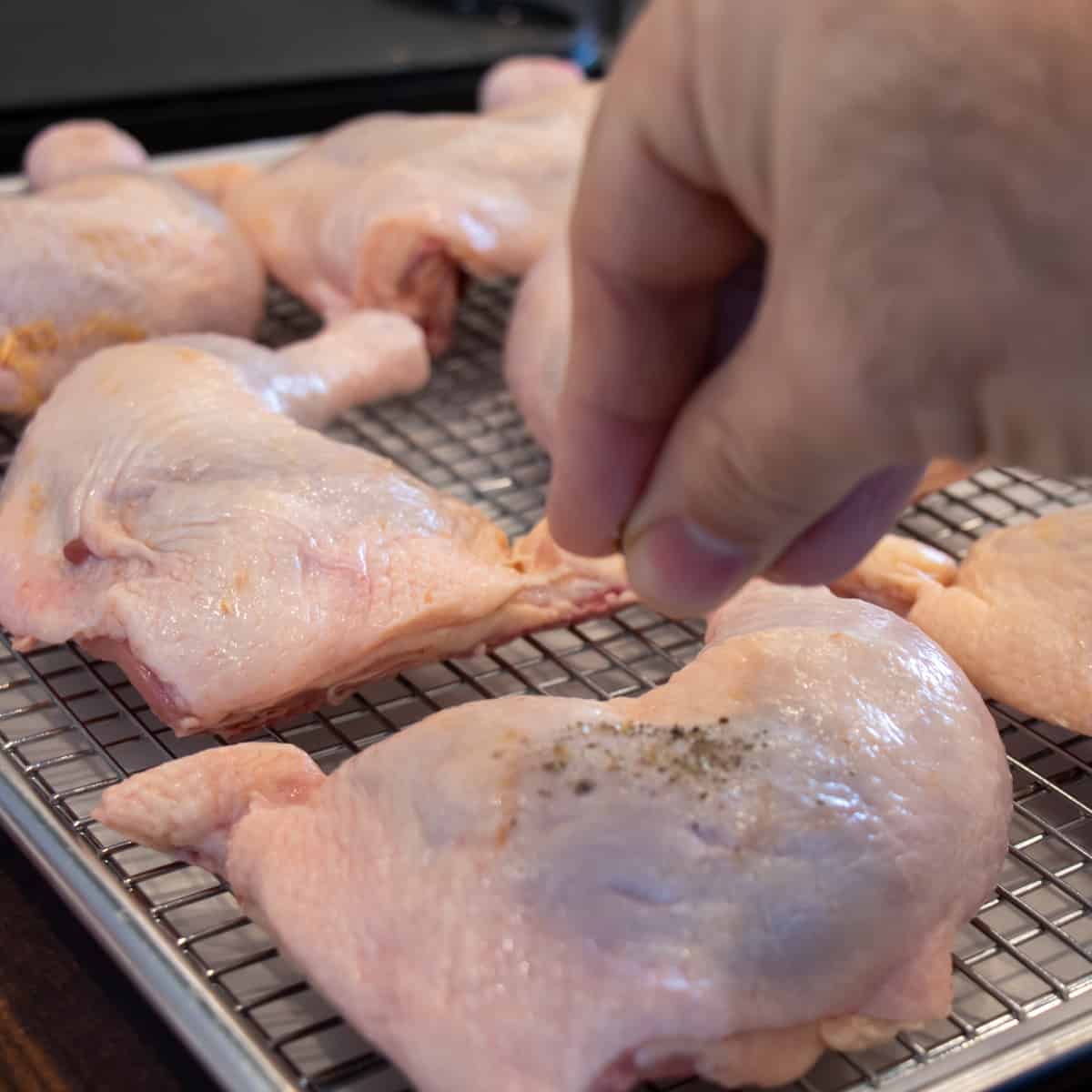 Action shot of sprinkling seasoning on a raw chicken piece.