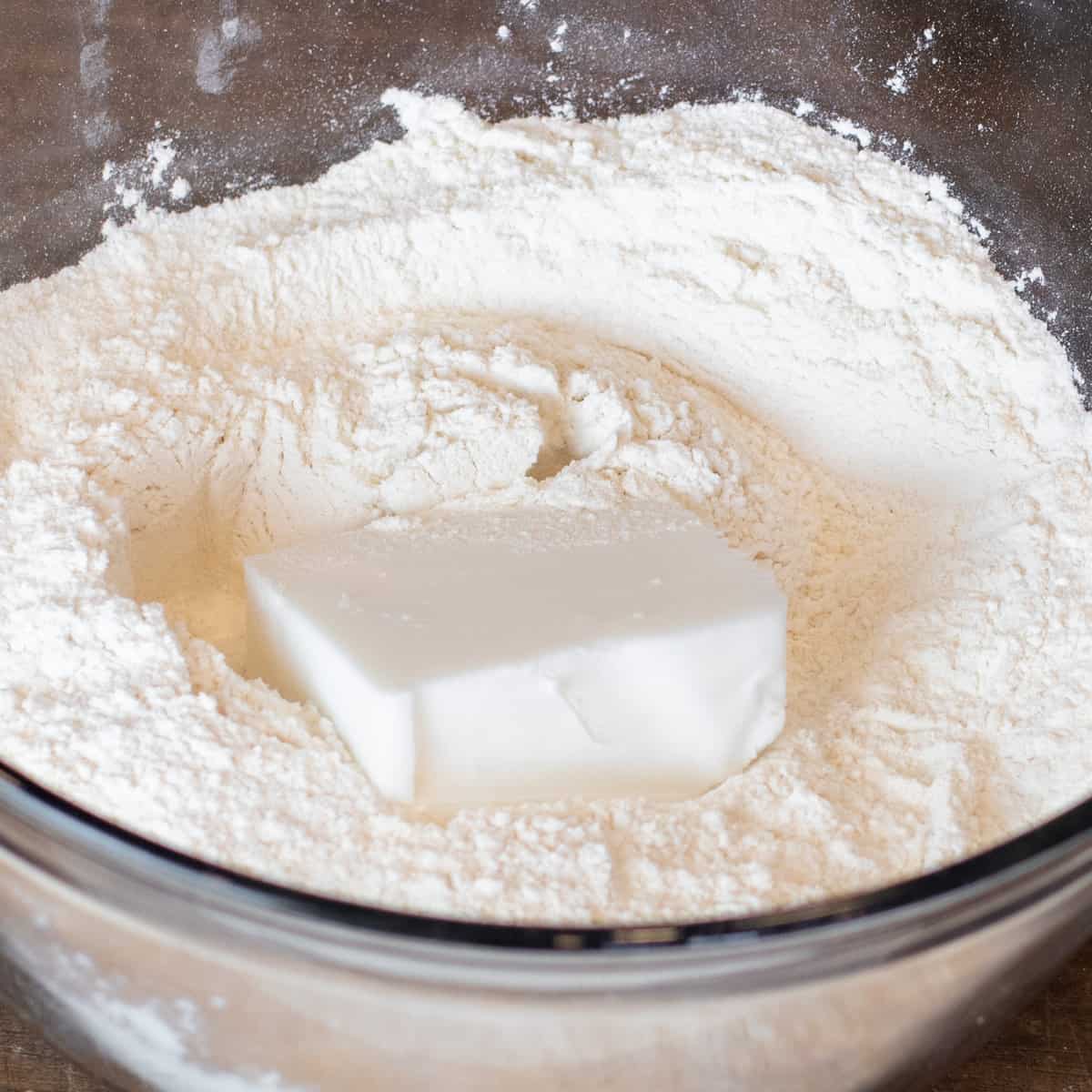 A portion of lard on some flour and sugar in a glass mixing bowl.