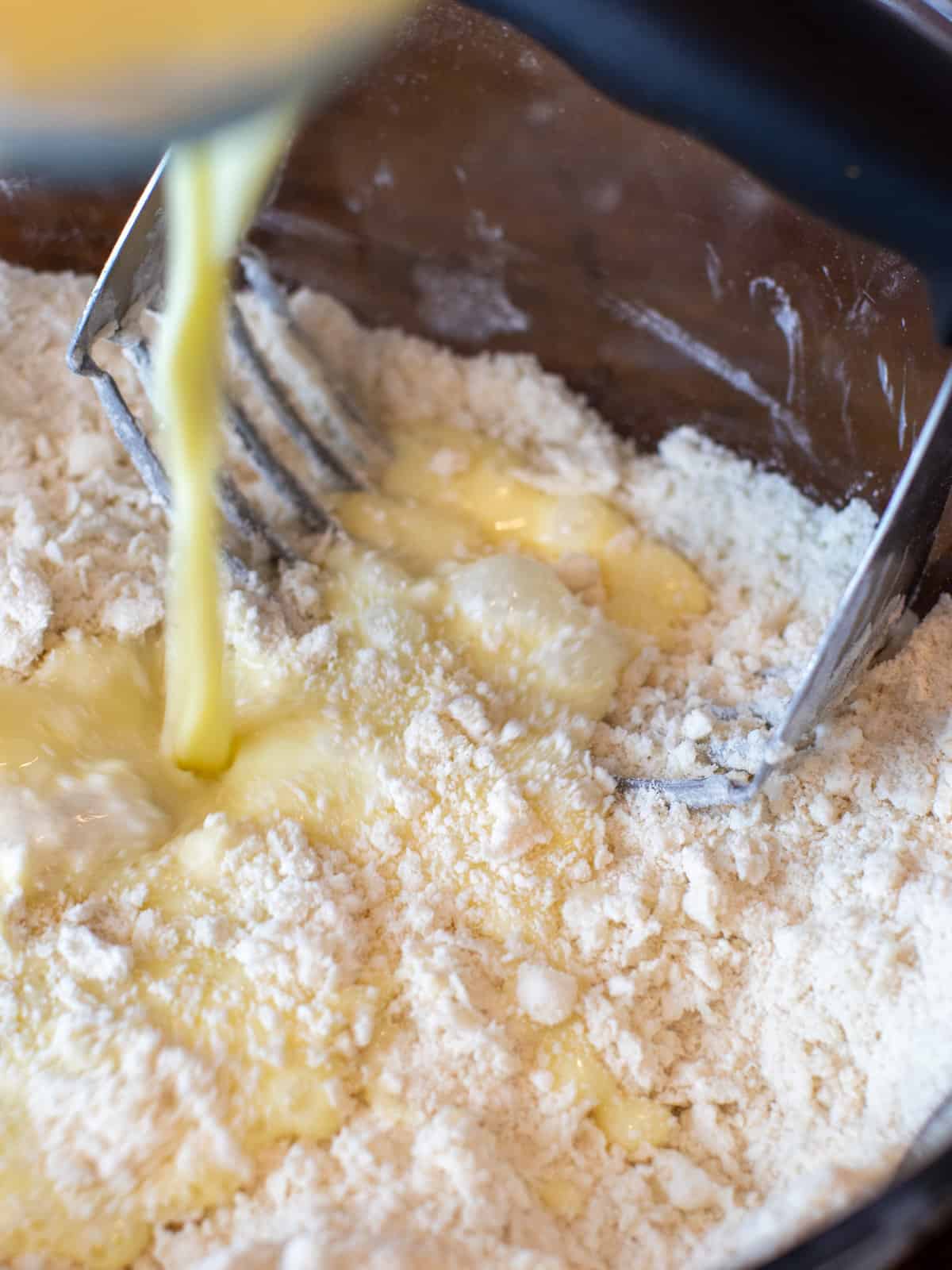 Egg and milk mixture being poured into the mixing bowl with dry ingredients.