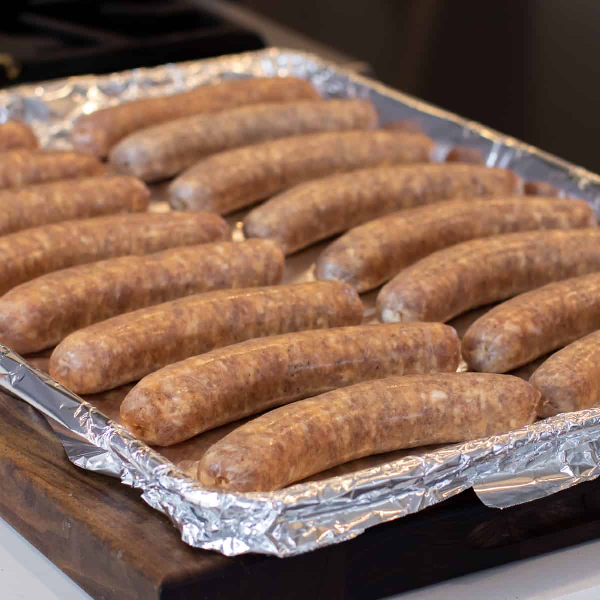 Raw sausages placed on a baking sheet lined with foil.