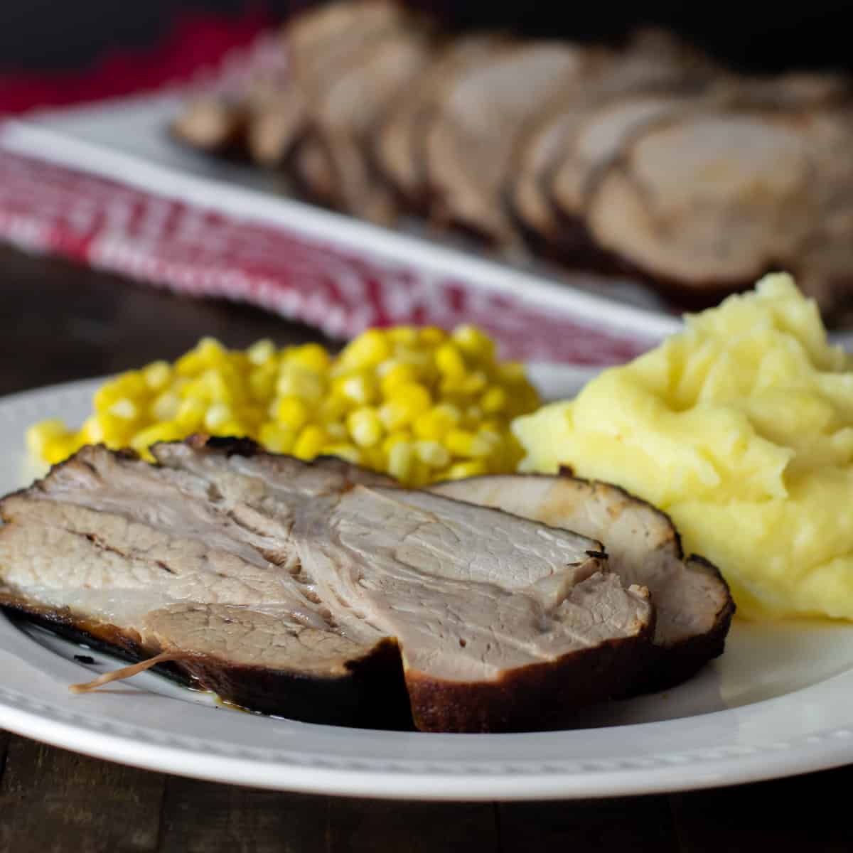 Close up picture of a dinner plate with pork roast, mashed potatoes and corn.