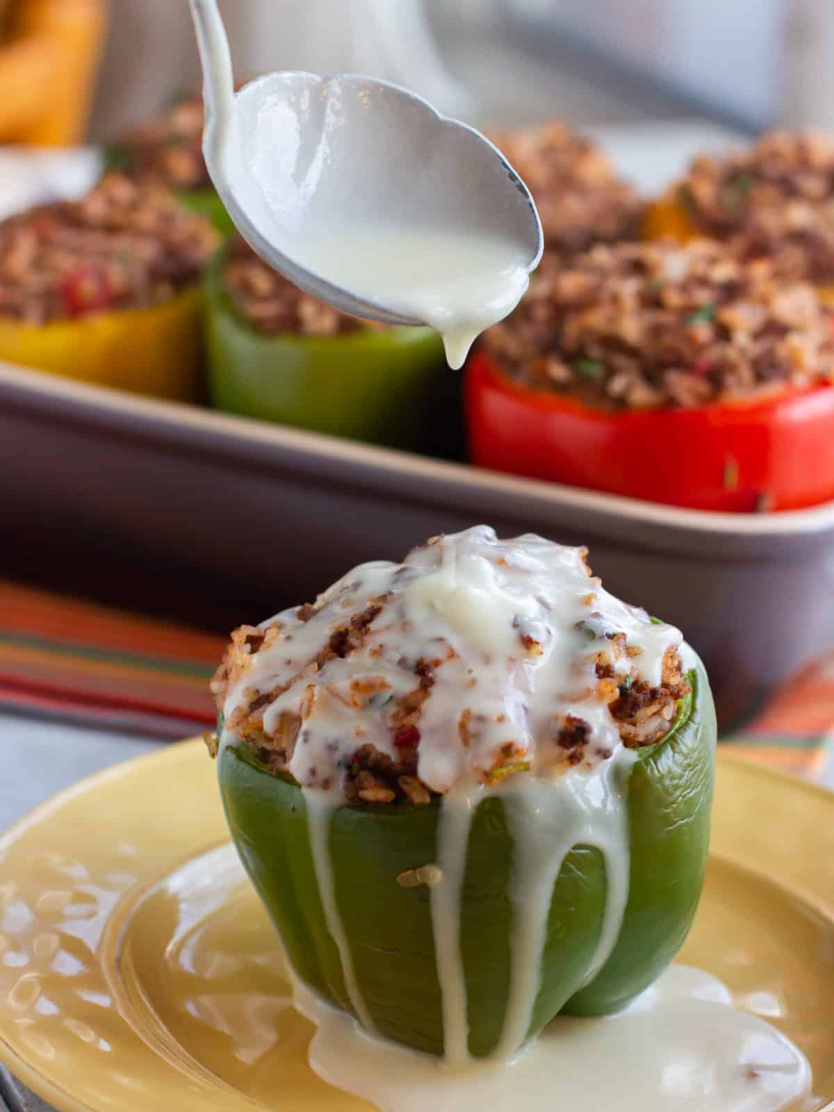 White cheddar cheese sauce being poured over a stuffed pepper.